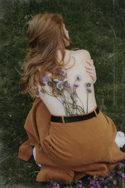 A woman with flowers on her back, embracing nature in a tranquil setting.