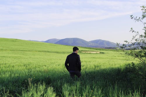 A Man in Black Jacket Walking on Green Grass Field