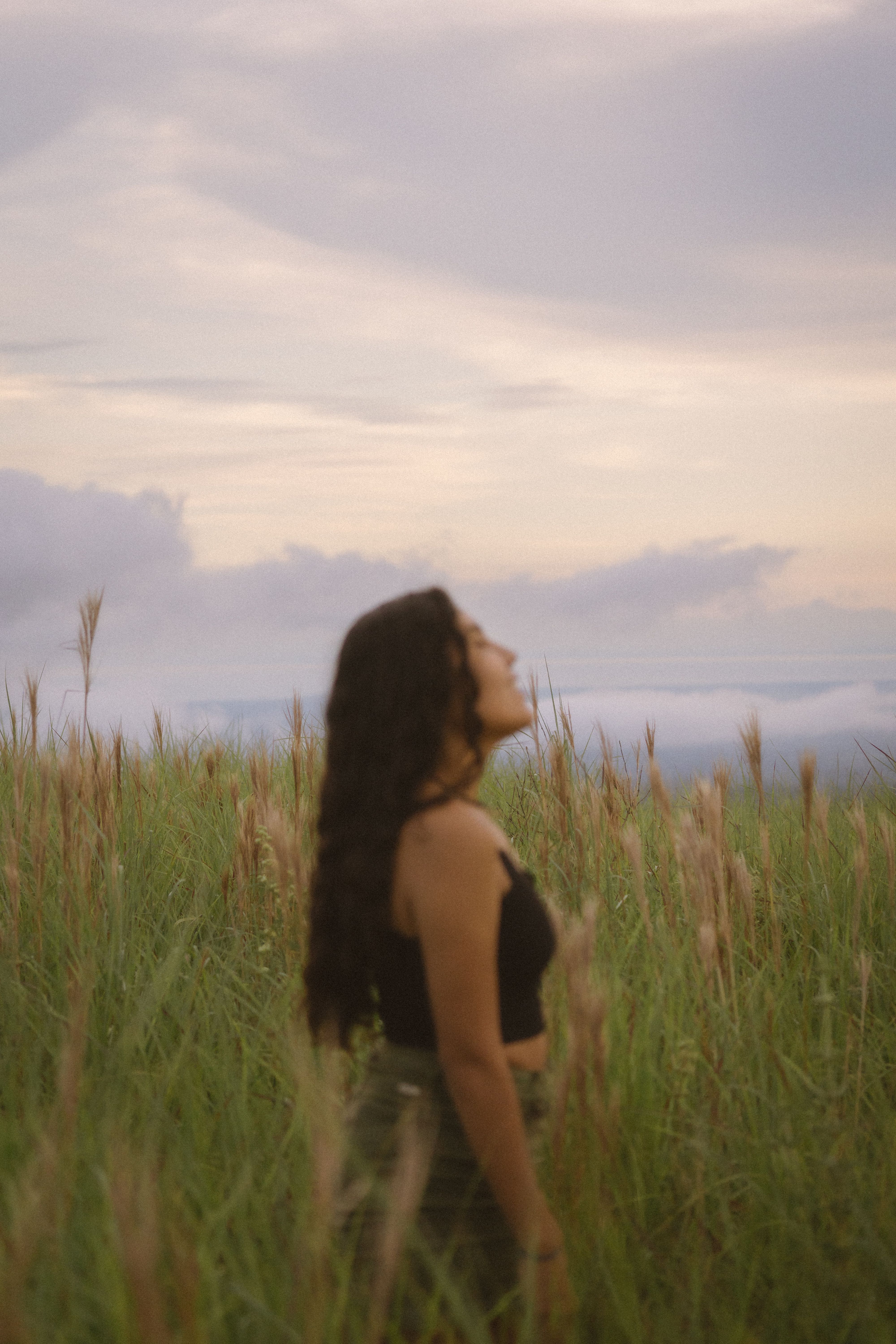 A serene moment captured of a woman standing in a lush grass field at sunset in Anton Valley, Panama.