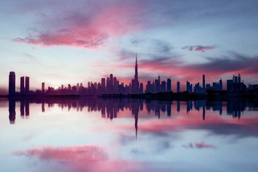 Captivating view of Dubai skyline with vibrant sunset and reflections in tranquil water.