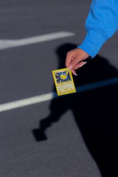 A hand in a blue sleeve holding a Pikachu Pokemon card against an outdoor background.