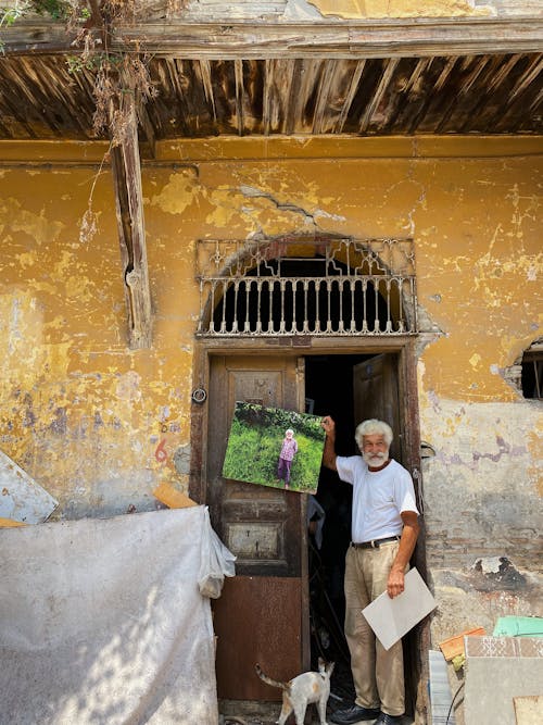 An Elderly Man Standing on an Old Wooden Door while Holding a Picture