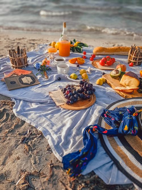 Free Vibrant picnic setup with fruits, drinks, and snacks on a beach shore, perfect for a summer day. Stock Photo