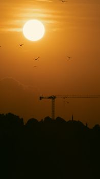 Dramatic silhouette of a crane against a vivid sunset with birds in the sky, creating a serene landscape.