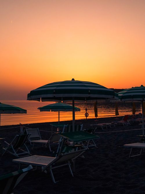 Free Scenic view of beach umbrellas silhouetted against a vibrant sunset in Praia A Mare, Italy. Stock Photo