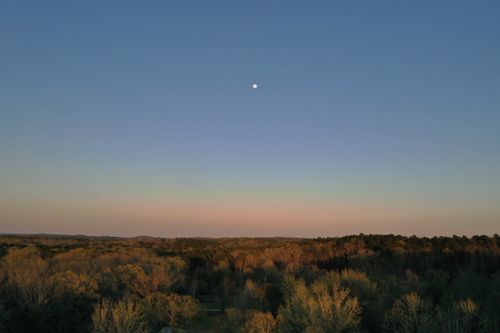 Free Aerial view of Benton, AR forest with moonrise under a clear blue sky. Stock Photo