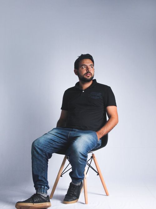 Free Portrait of a fashionable man sitting on a chair in a modern studio setting with a neutral gray background. Stock Photo