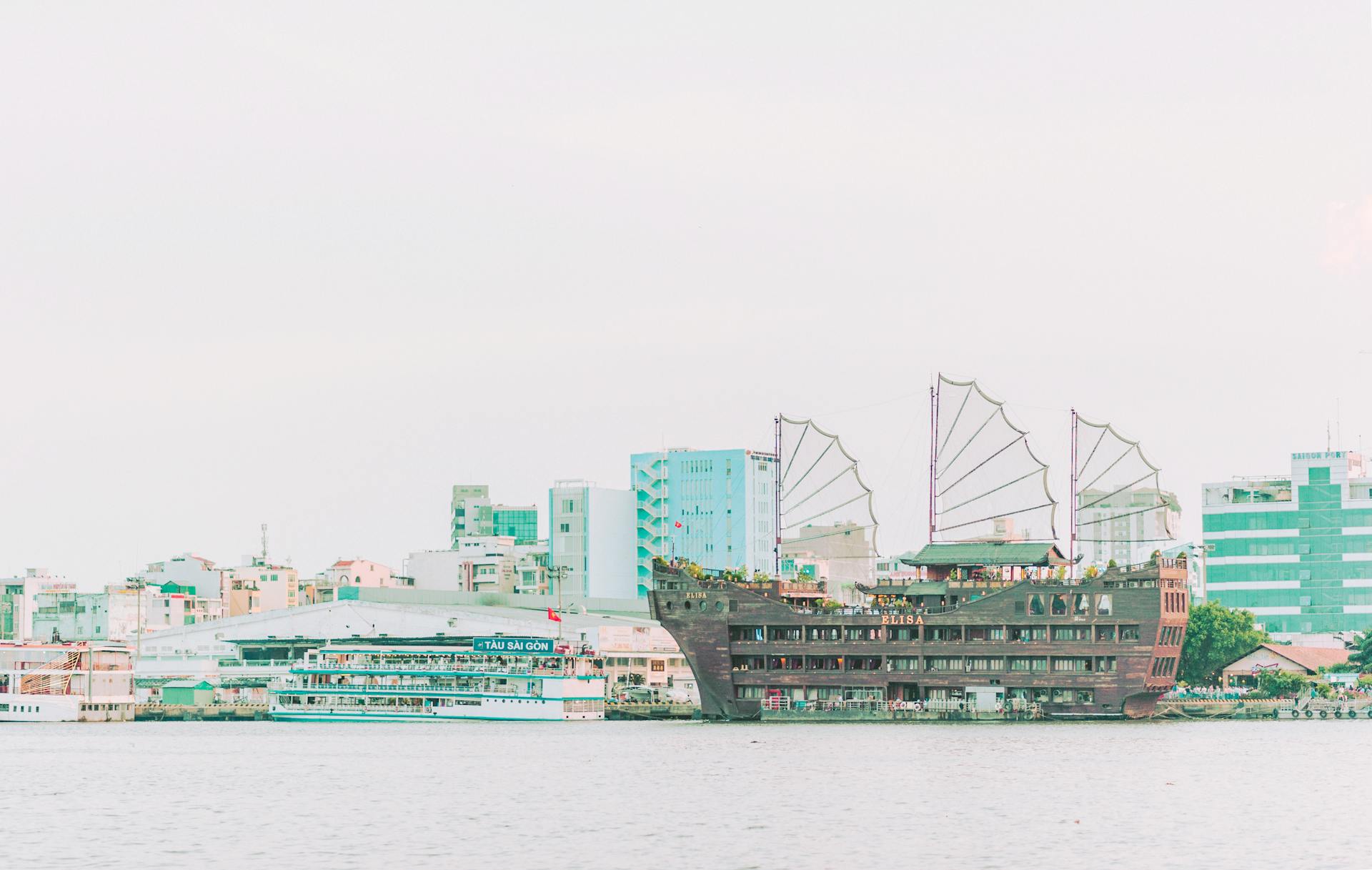 Scenic view of a city harbor with a distinctive ship and modern buildings across a calm river.