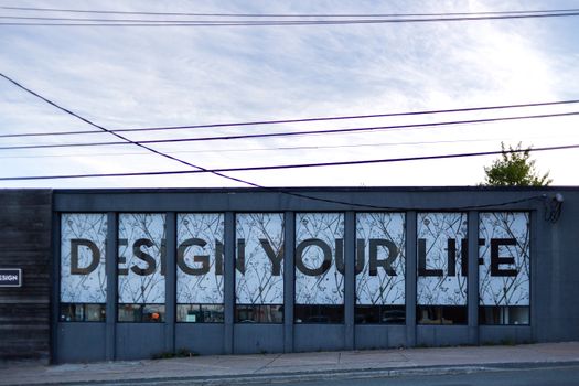 Modern storefront featuring glass windows with 'Design Your Life' signage against a clear sky.