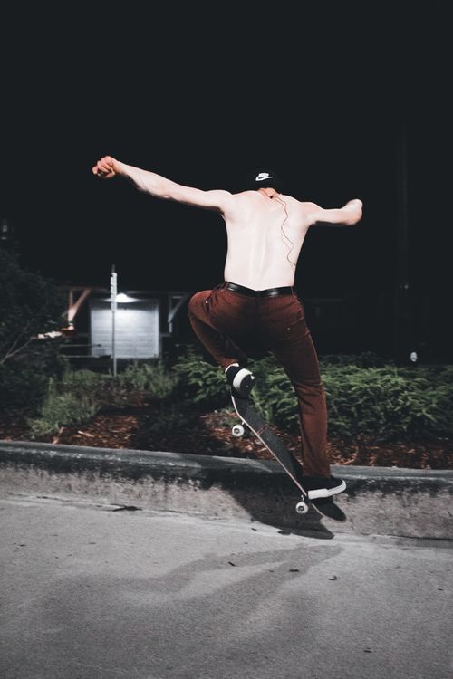Free Shirtless skateboarder midair while doing a trick on a street curb at night. Stock Photo