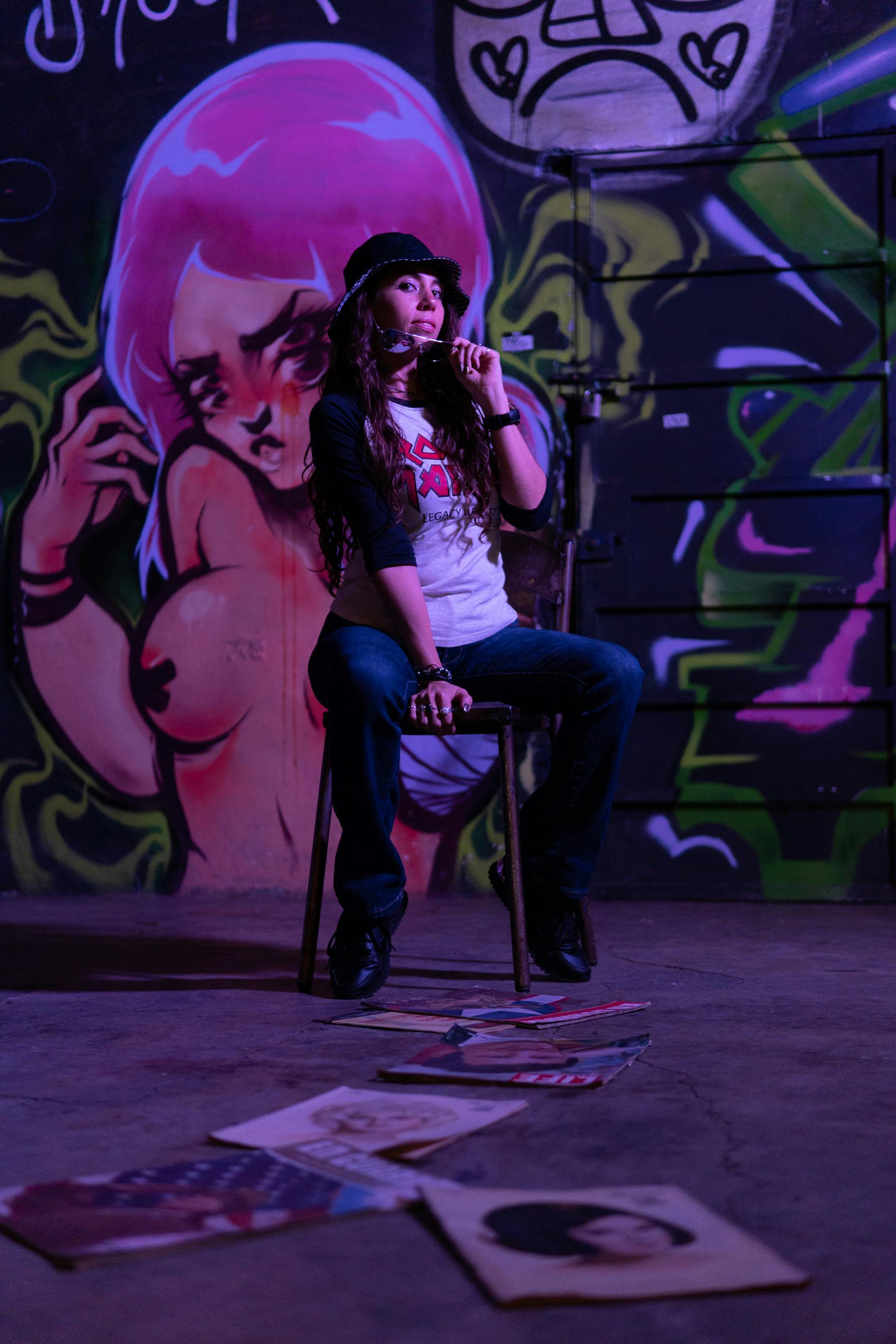 a woman sitting in a chair beside a wall with graffiti