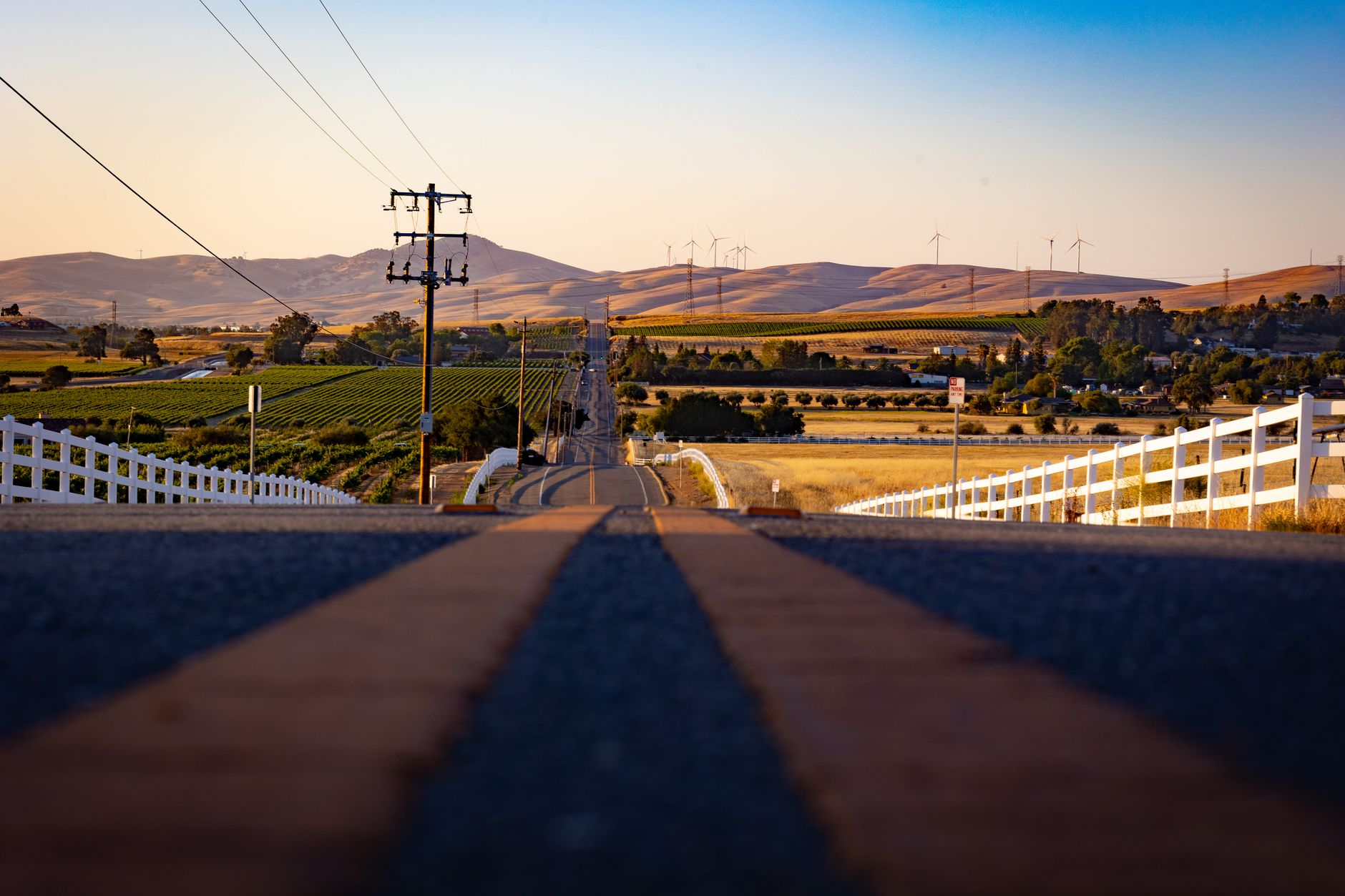 A picturesque view of a country road in Livermore, CA with vineyards and windmills at sunset.
