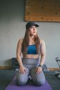 Woman in Blue Tank Top and Gray Leggings Wearing Black Fedora Hat Sitting on Gray Chair