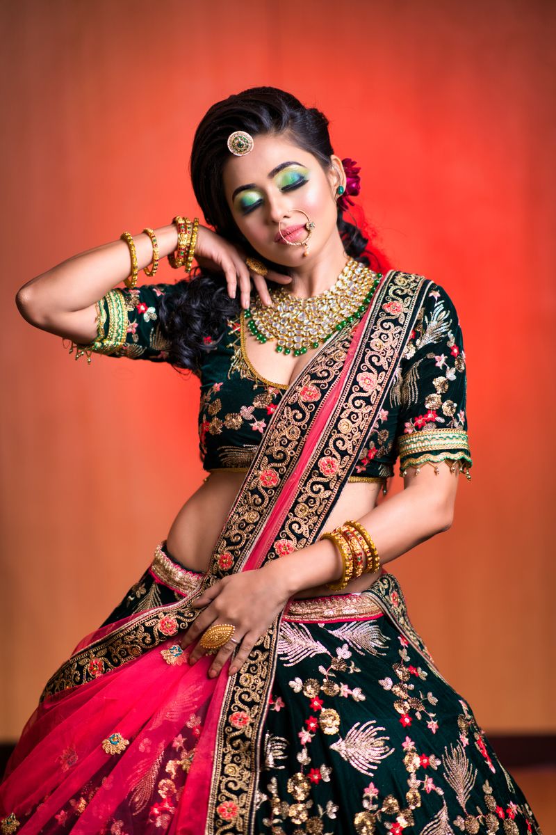 Indian woman posing gracefully in floral embellished lehenga against orange background.
