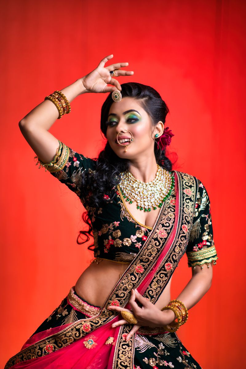 A joyful Indian woman in traditional bridal wear dances gracefully against a vibrant red background.