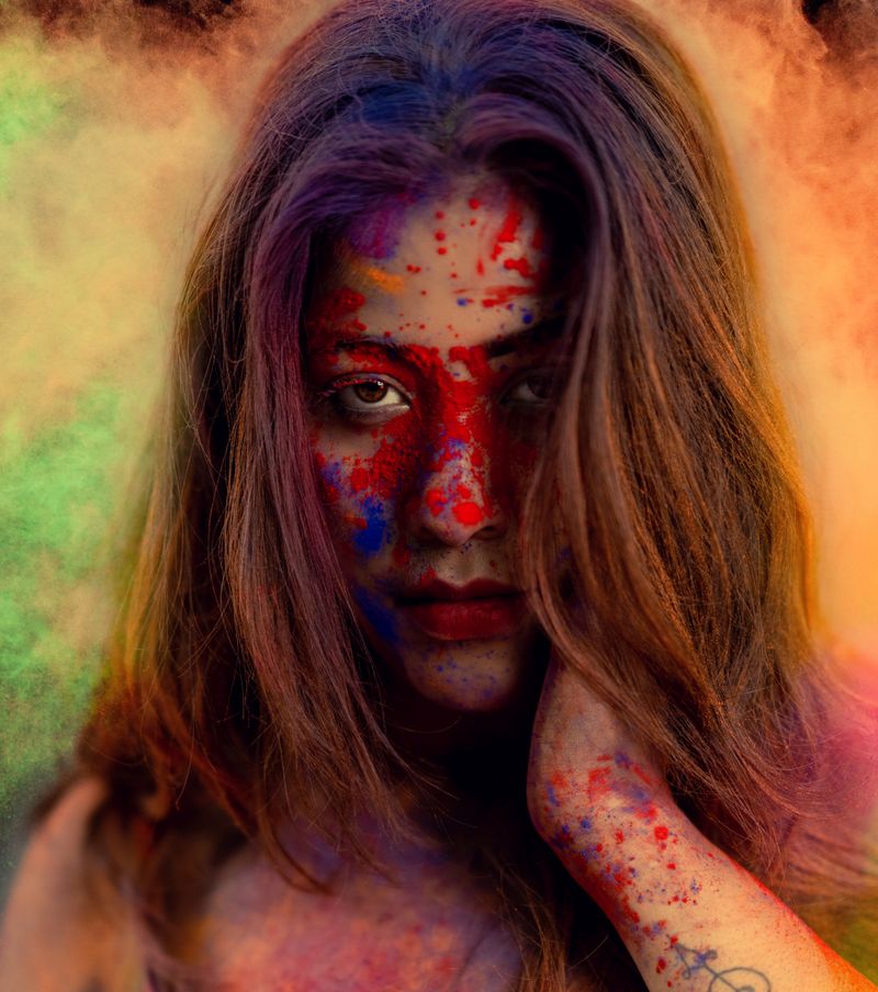 Close-up portrait of a woman with vibrant face paint and colorful smoke backdrop.