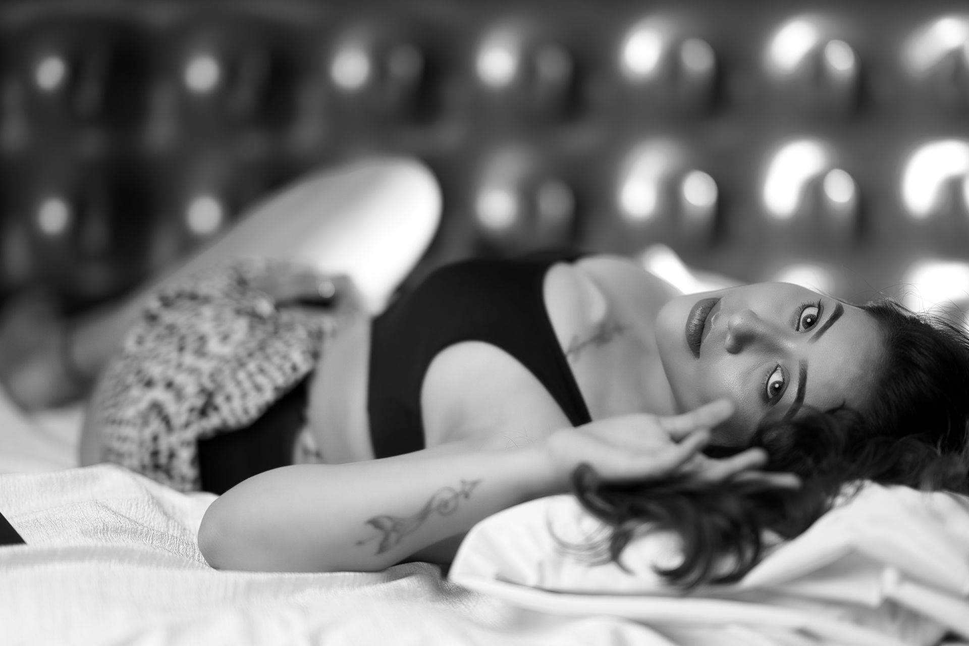 A woman in a black tank top posing gracefully on a bed in classic black and white.