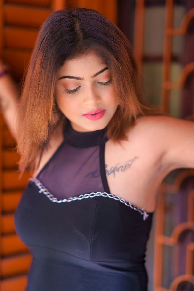 Portrait of a woman in a black dress showcasing her tattoo in an indoor setting.