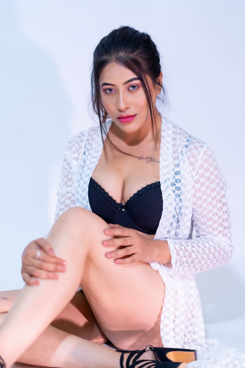 Stylish woman in black lingerie posing in a studio setting against a white background.