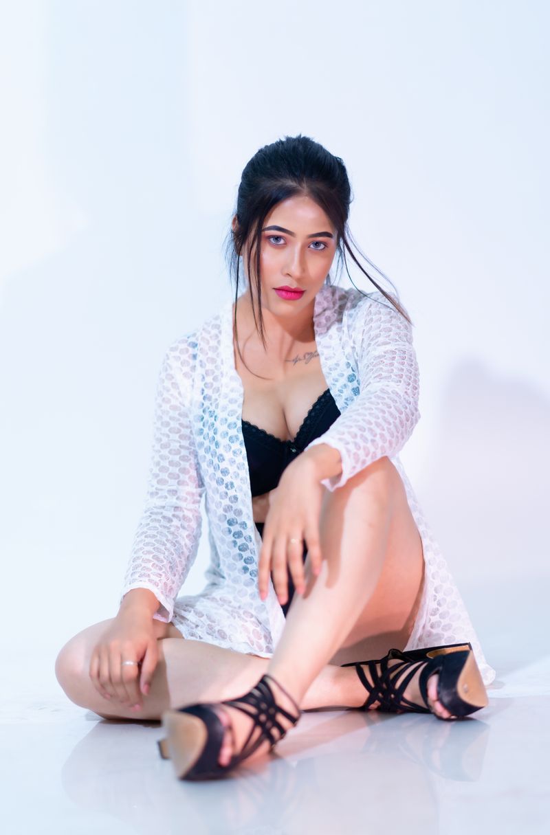 A stylish woman sits confidently on the floor wearing a white lace cover-up and black top.