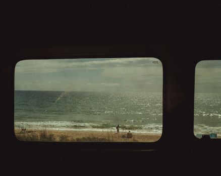 Scenic view of the ocean and beach framed by a vintage train window, evoking summer vibes.