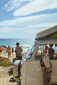 A classic van parked on a beach with people enjoying a sunny day by the sea.