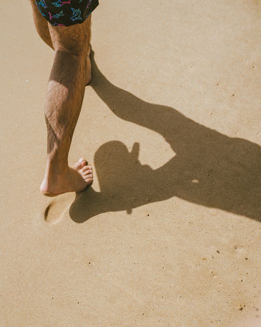 A person walking barefoot on a sunny sandy beach, casting a shadow. A person walking barefoot on a sunny sandy beach, casting a shadow.