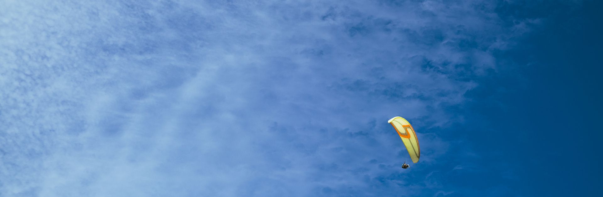 A paraglider soars through a vibrant blue sky dotted with clouds, capturing the thrill of air sports