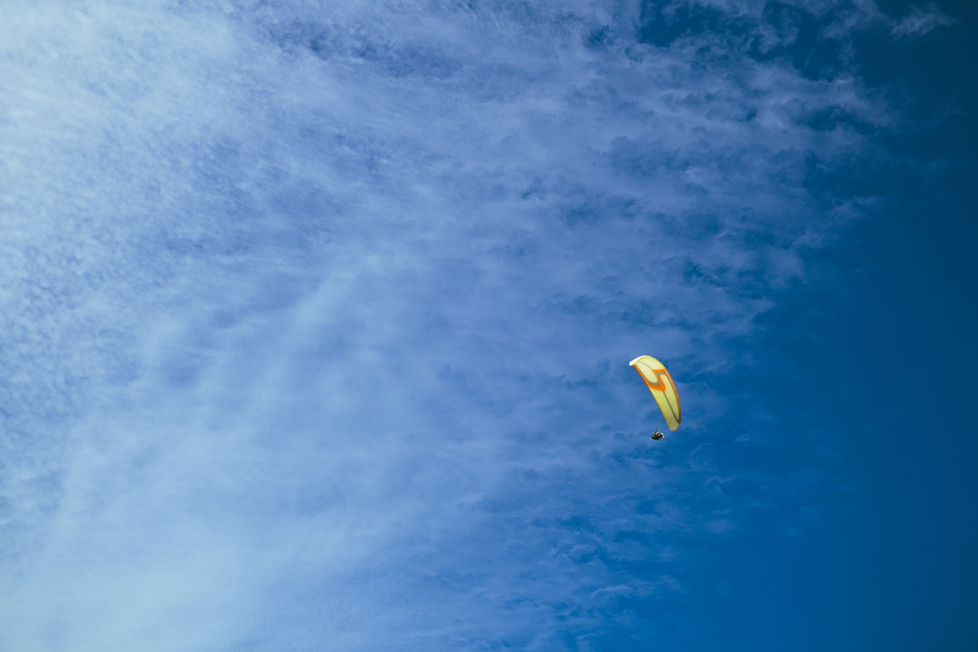 A paraglider soars through a vibrant blue sky dotted with clouds, capturing the thrill of air sports