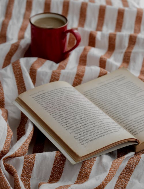 Open Book Beside a Cup of Coffee on Top of a Blanket