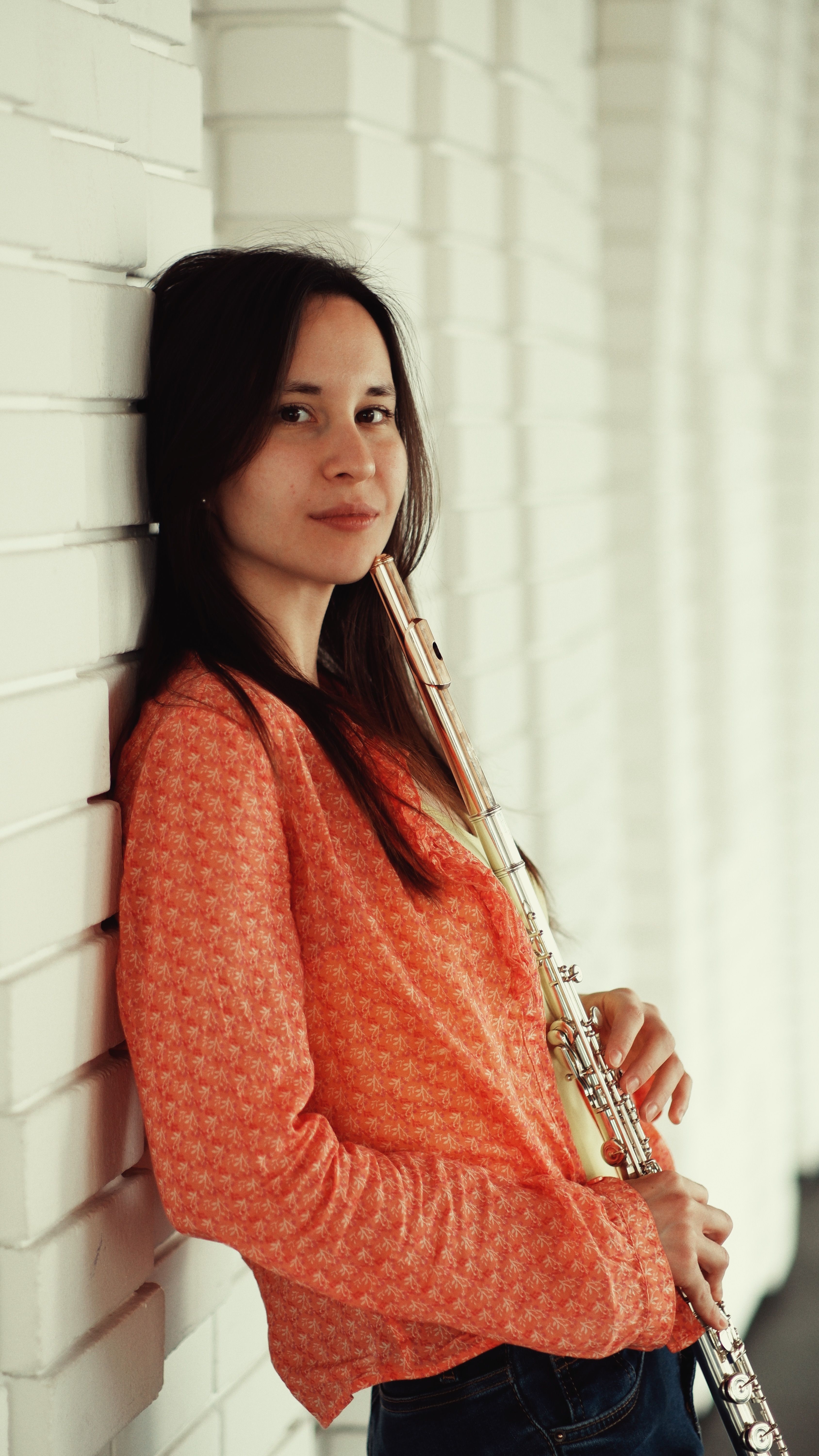 Portrait of a young woman leaning against a wall with her flute, exuding elegance and passion for music.