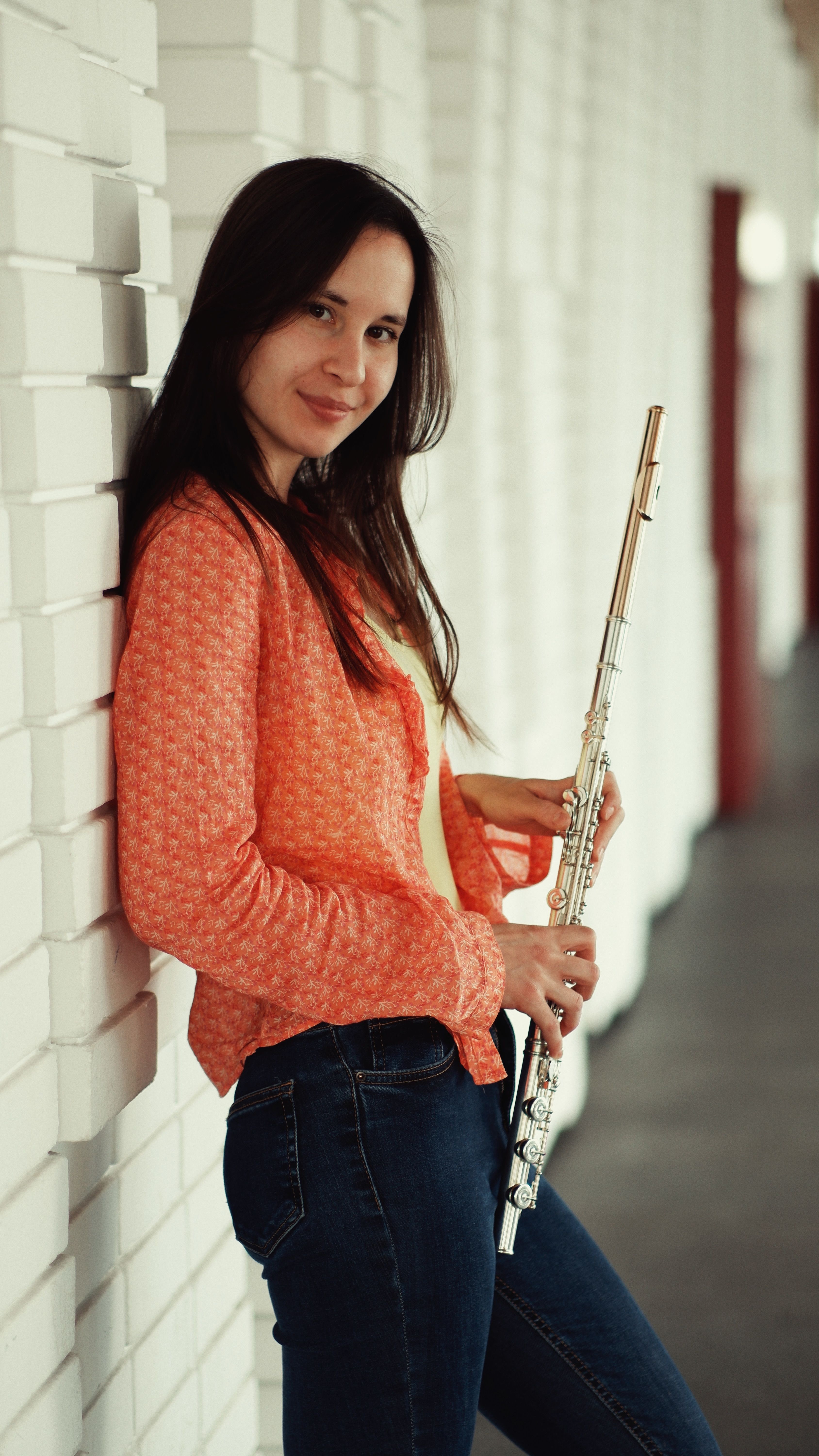 Portrait of a young woman with a flute, smiling against a stylish brick wall.