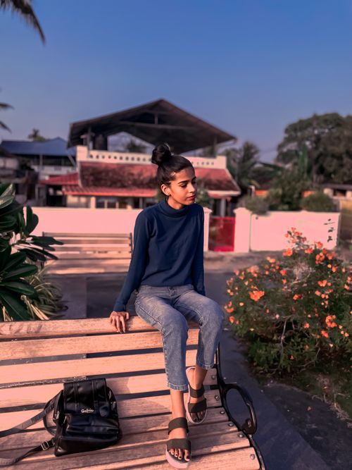 Free A young woman in casual attire sits on a bench outdoors, enjoying a calm day. Stock Photo