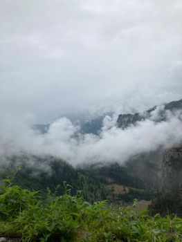 Breathtaking view of fog-covered mountains in Kullu, India, showcasing lush greenery and a serene atmosphere.