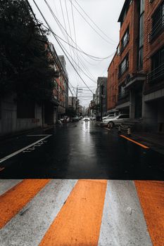 Rainy day view of a city street lined with brick buildings and parked cars.