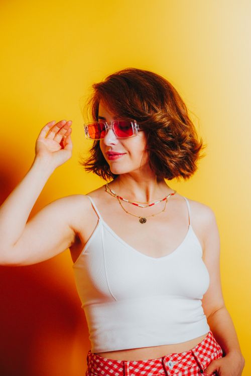 Free Stylish woman in colorful sunglasses posing playfully with a vibrant yellow backdrop. Stock Photo