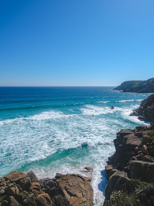 Free Stunning view of blue ocean waves crashing against rocky coastline under a clear blue sky. Stock Photo