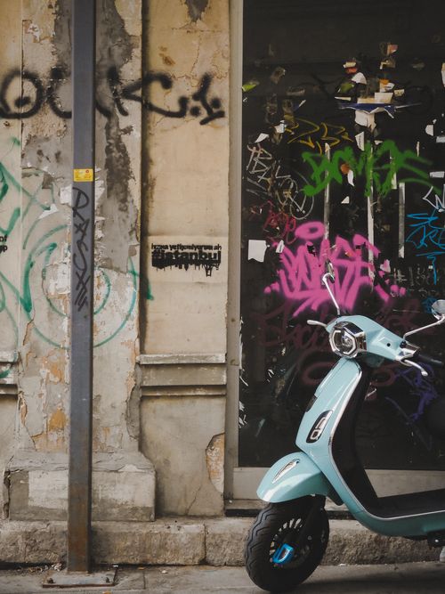 Free Vintage motor scooter parked beside a graffiti-covered wall on a city street. Stock Photo