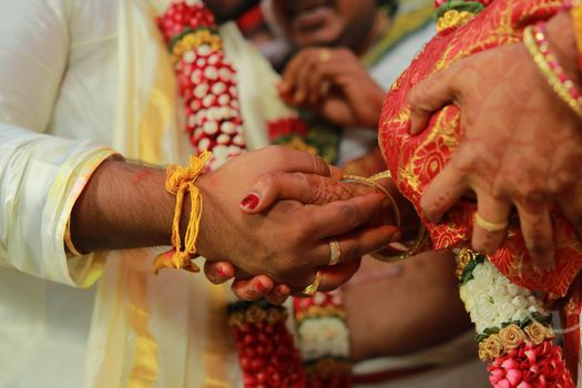 Close-up of hands during a traditional Indian wedding ceremony, showcasing rituals and vibrant attire.