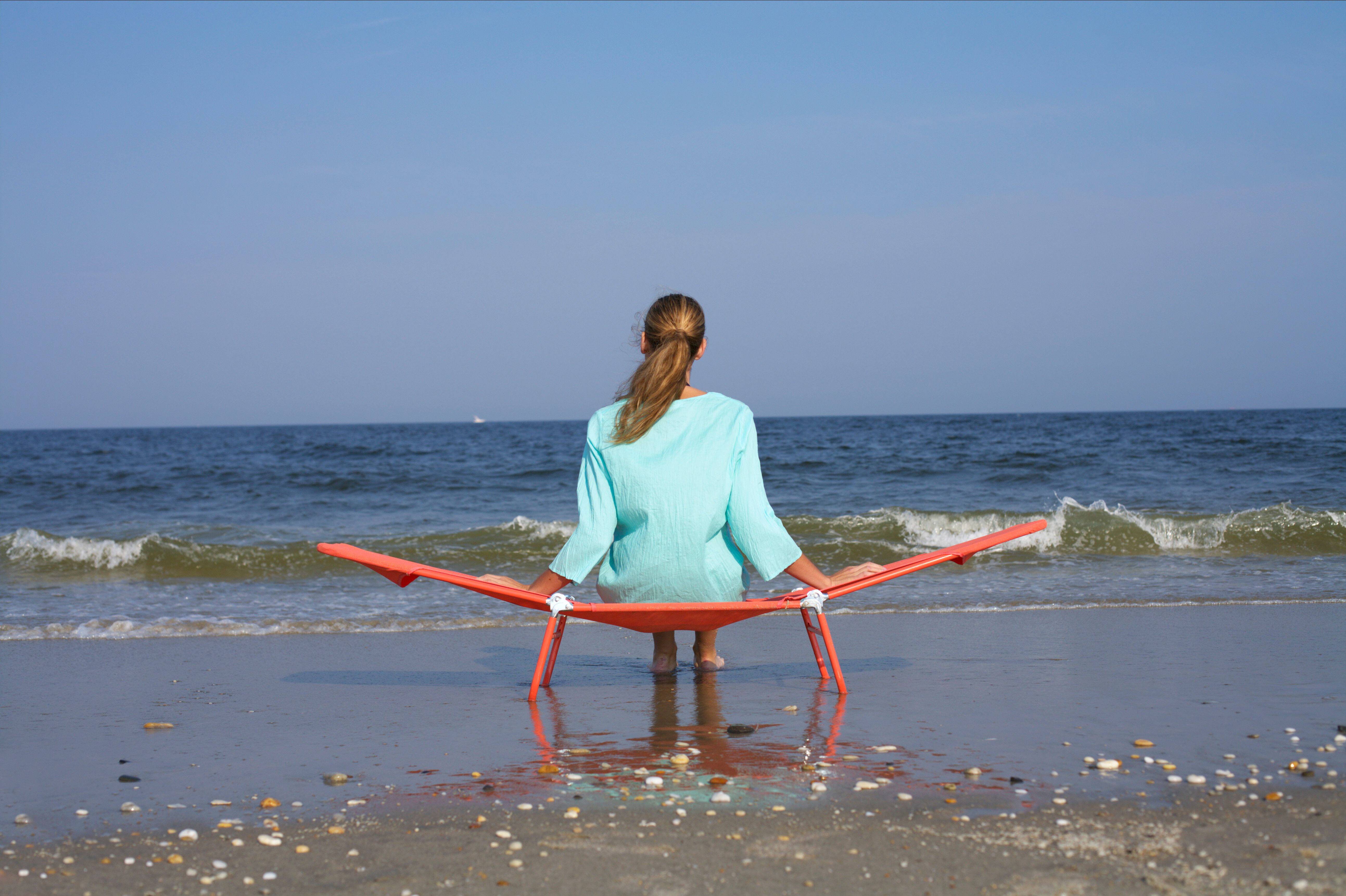 Woman lounging on a beach chair facing the ocean, enjoying a sunny day by the seashore.