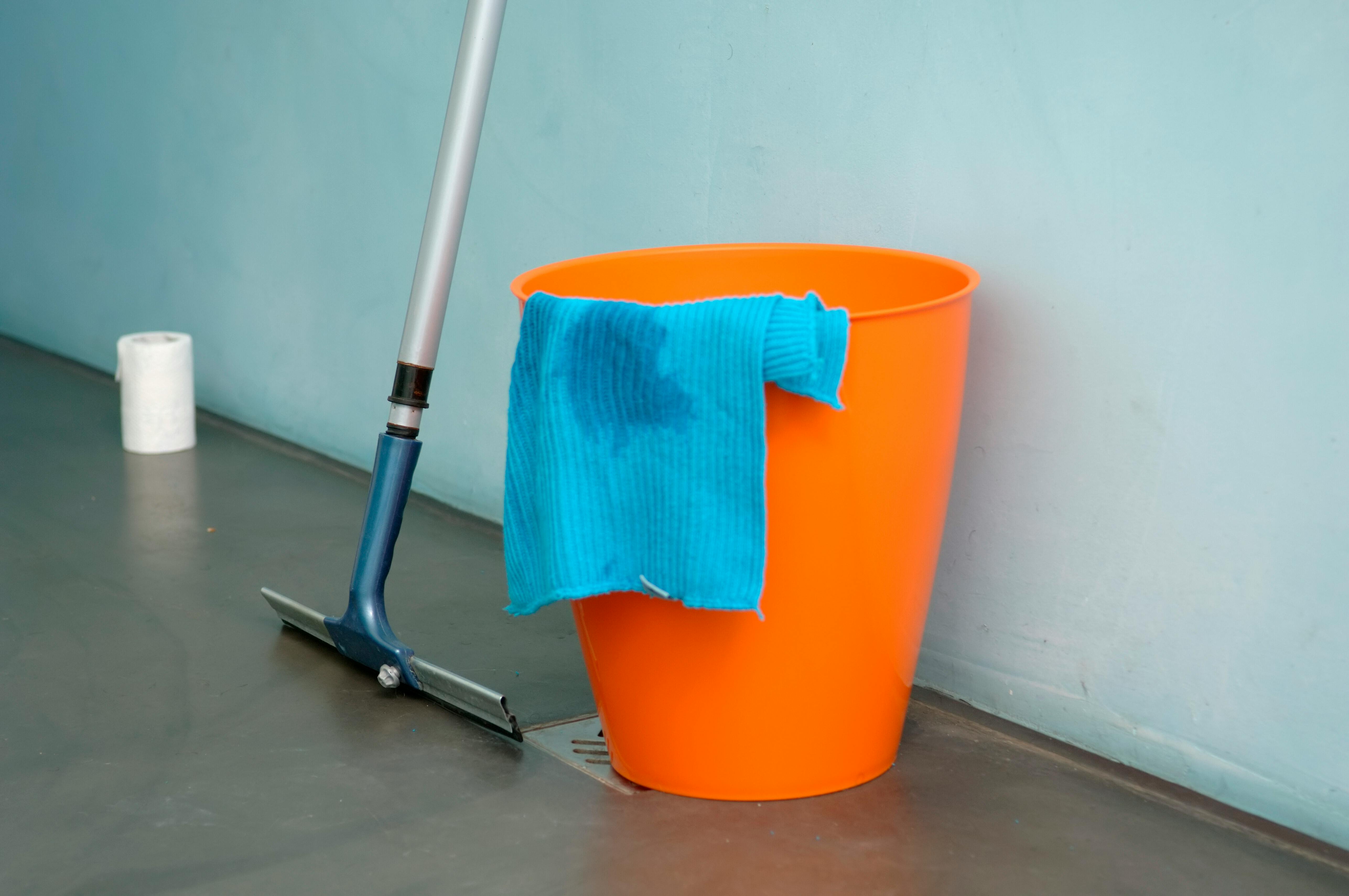 Free Close-up of cleaning supplies including orange bucket, mop, and blue rag indoors. Stock Photo