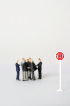 Close-up of miniature business figures gathered near a small stop sign on a white background.