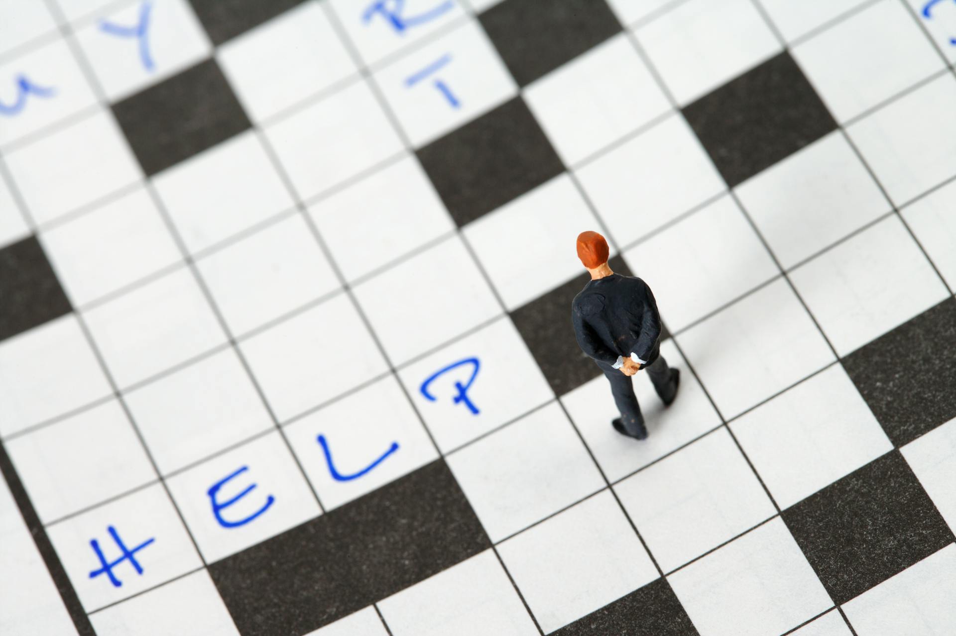 Tiny figurine searching for answers on a crossword puzzle with 'Help' written.