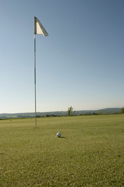 Fotomural Una vista serena de un campo de golf con un banderín y una bola de golf bajo un cielo despejado.
