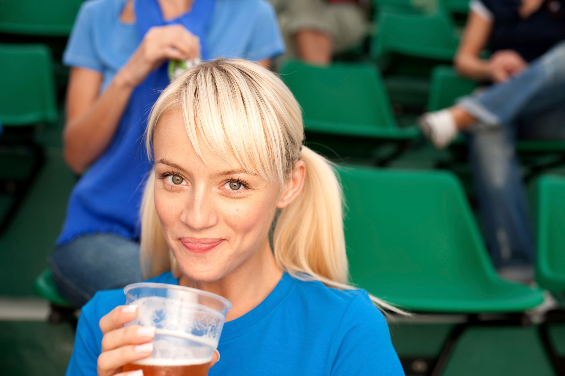 A cheerful woman enjoying a drink while seated at an outdoor event.