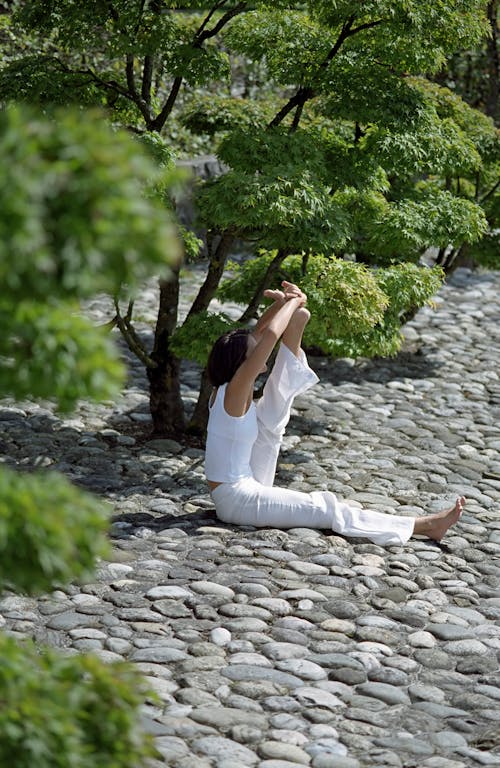 Woman in White Tank Top and White Pants Sitting on Gray Concrete Pavement