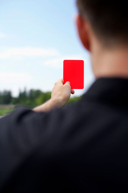 Rear view of a referee holding up a red card during a soccer match outdoors.