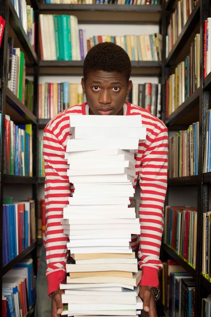 Student carrying heavy stack of books in library, focused on education. Student carrying heavy stack of books in library, focused on education.
