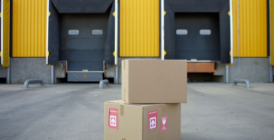 Cardboard boxes stacked at a warehouse loading dock — cartons and returnable crates are how cockroaches travel between outlets