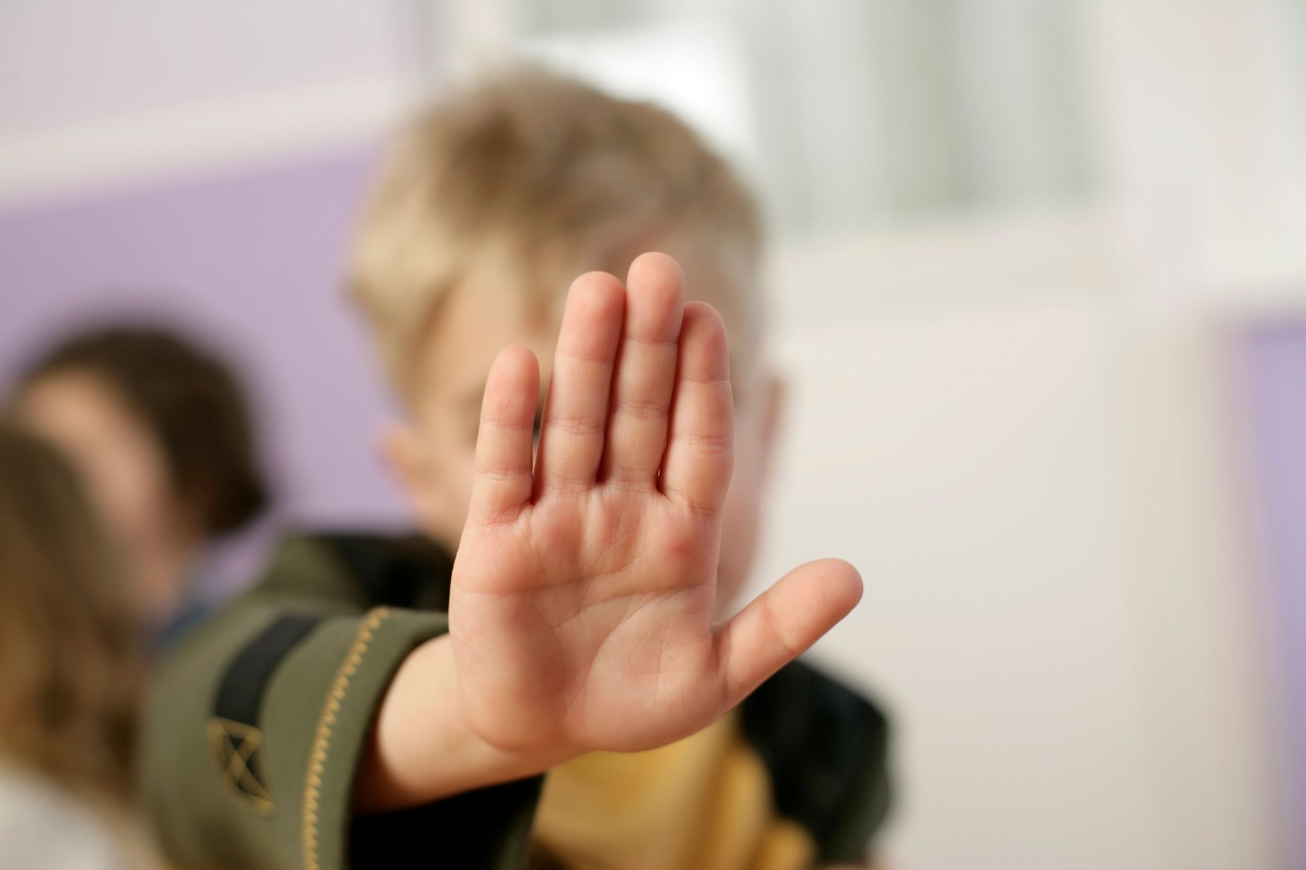 A child making a stop gesture with an open hand indoors.